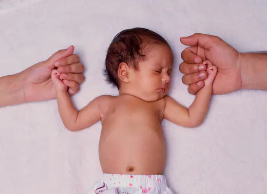 Newborn baby holding the fingers of both parents